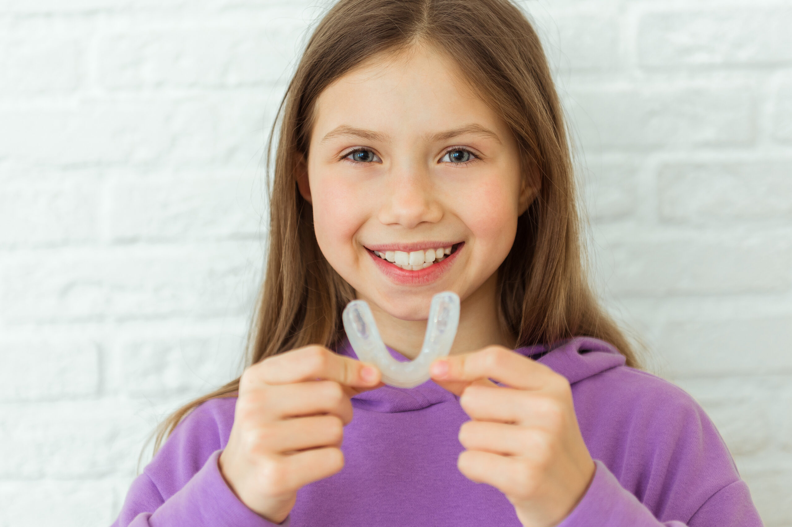 Positive child girl holds mouth guards for her teeth. Orthodontic silicone transparent teeth aligner in female hands. Bracket for teeth whitening. Dental care